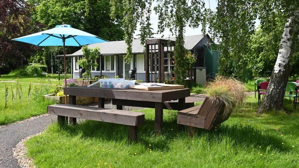 A wooden table with chairs and a bench in a garden.