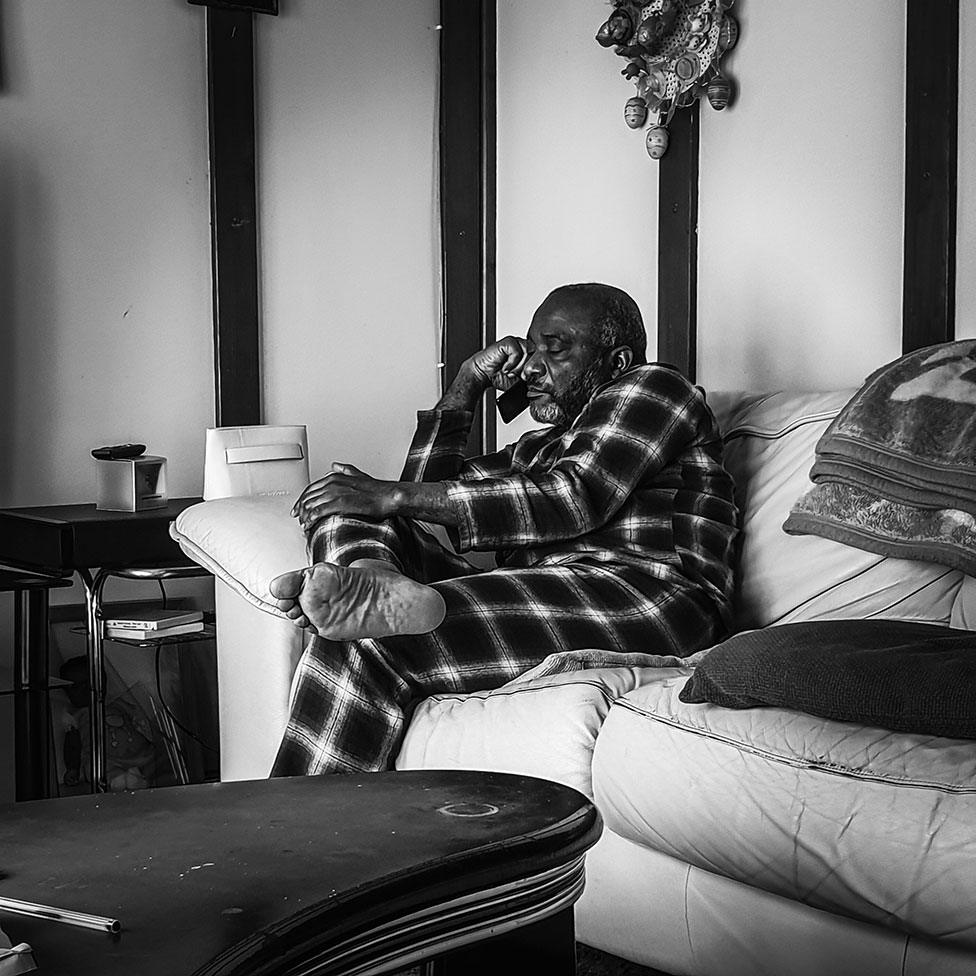 A man sits on the sofa with a mobile phone to his ear