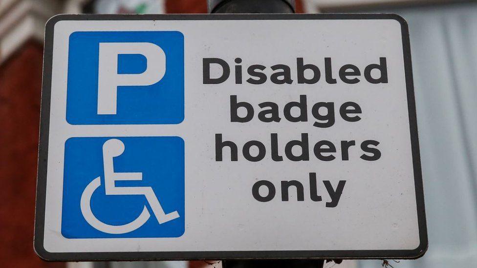 A parking sign stating "disabled badge holders only" in black text on a white background. To the left of the text are two parking symbols, a letter P and a wheelchair symbol, both in white on blue backgrounds.