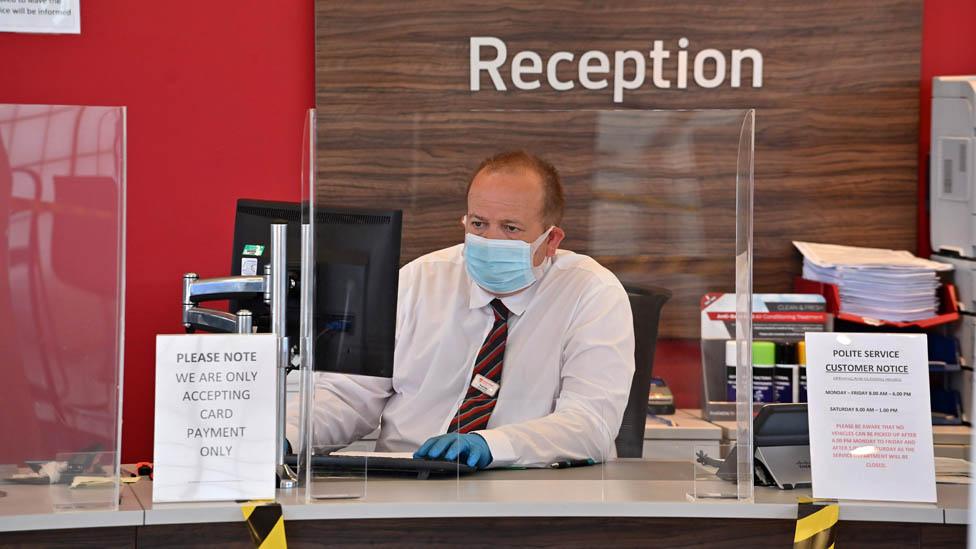 An employee wears PPE (personal protective equipment) including a face mask and gloves as a precautionary measure against COVID-19, as they sit behind perspex screen in the reception of a recently re-opened Vauxhall car dealership in north London