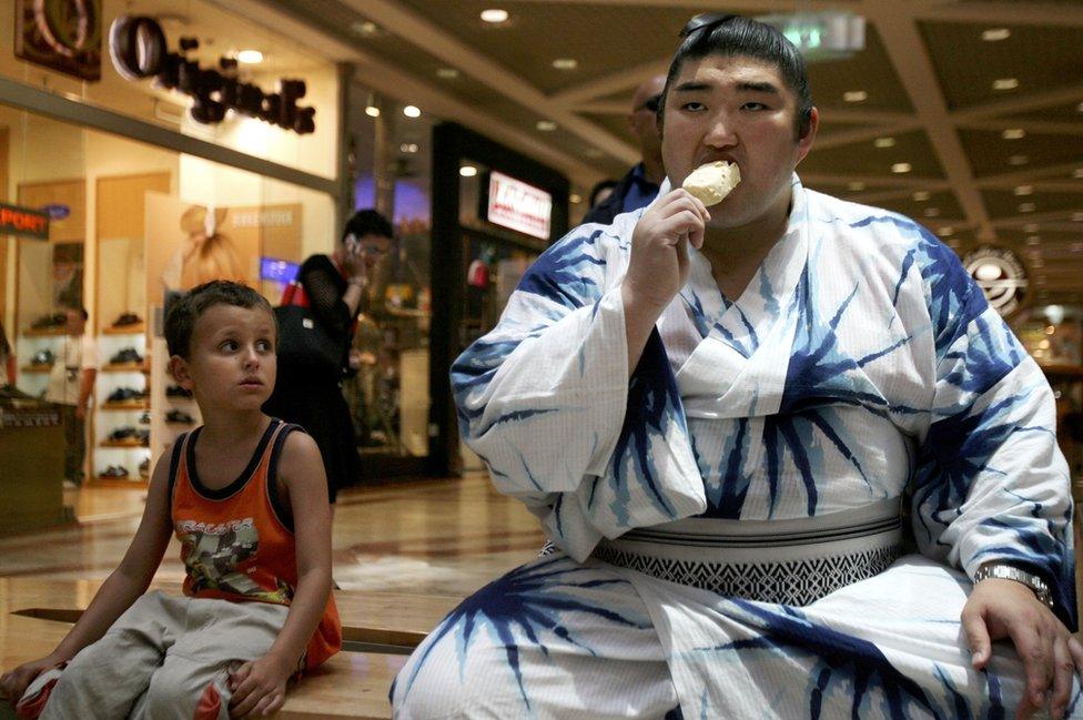 Japanese sumo wrestler Sekiwake Kotomitsuki eats ice cream while a little boy watches him during a visit to a Tel Aviv shopping centre