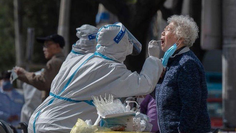 A health worker wears protective gear as she gives a nucleic acid test to detect COVID-19 on a local resident at a mass testing site after new cases were found, on April 6, 2022 in Beijing, China.