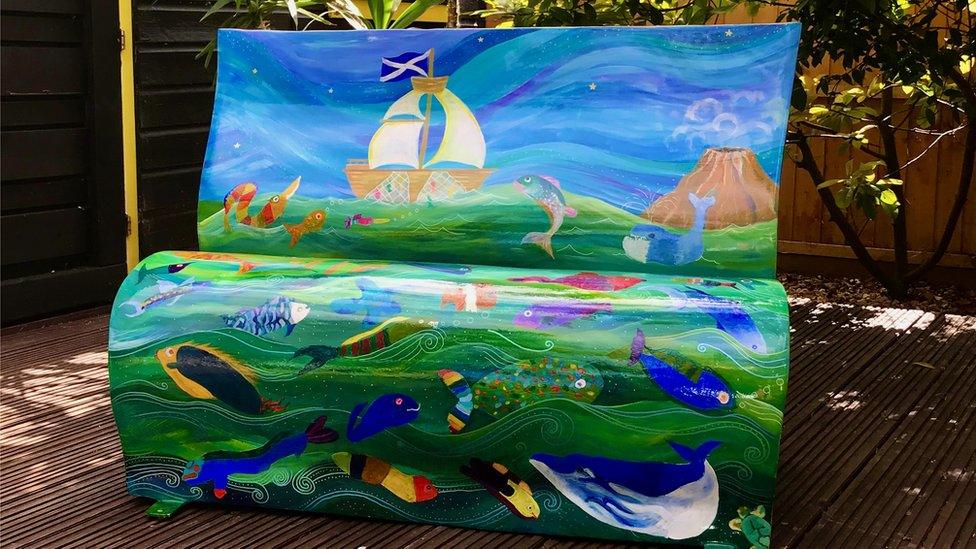 One of the benches decorated with a sea scene including a boat, fish and a volcano