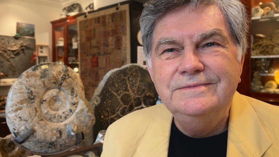 Wolfgang Grulke in his museum sitting next to a large ammonite