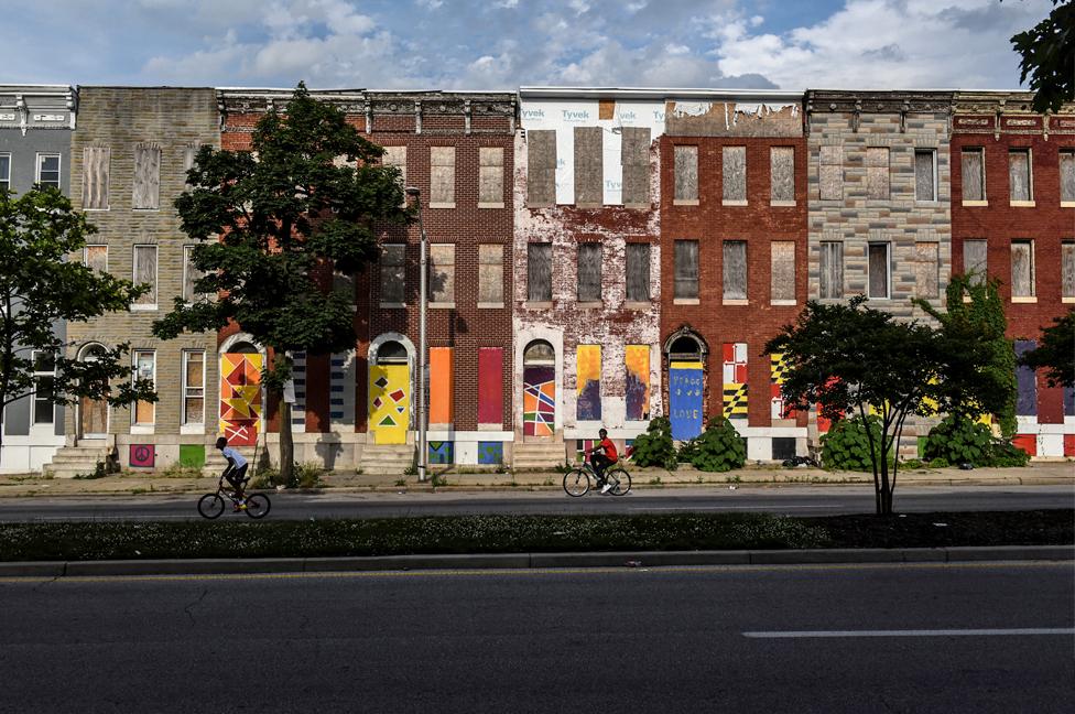 Young boys ride their bikes past a boarded-up and abandoned row of houses in Baltimore.