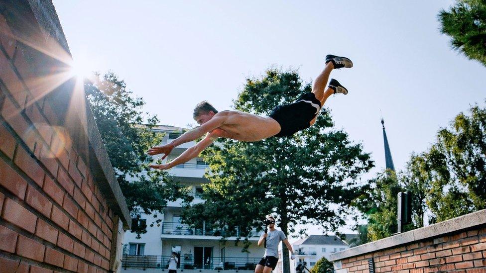 Man jumping between buildings with his arms outstretched