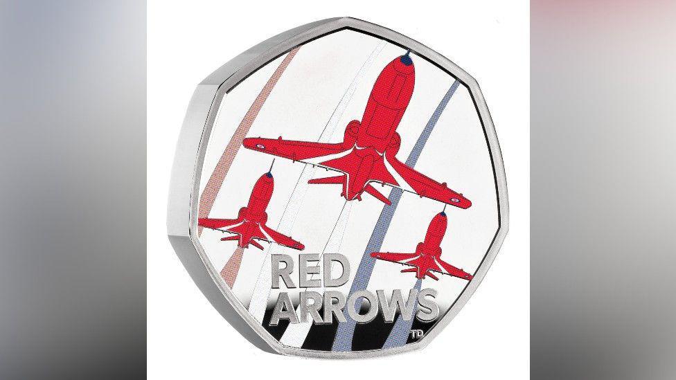 The 50p Red Arrows coin close up with a white background. There are three painted red T1 aircraft, with a larger one at the top and two underneath. There are blue and red lines coming from the aircraft. "Red Arrows" is written at the bottom.