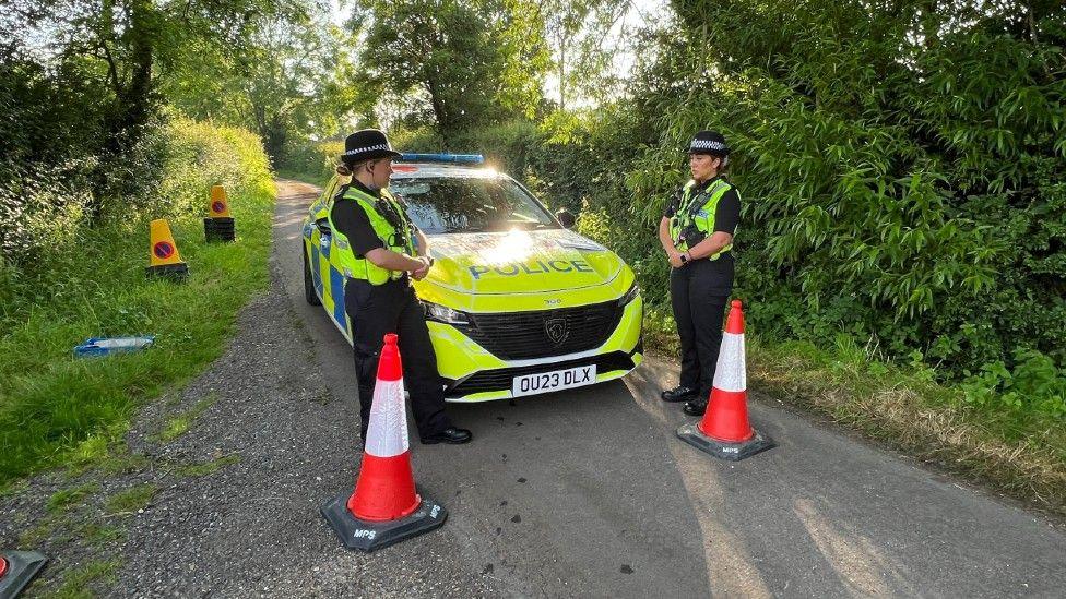 Two police officers stand in front of a police car