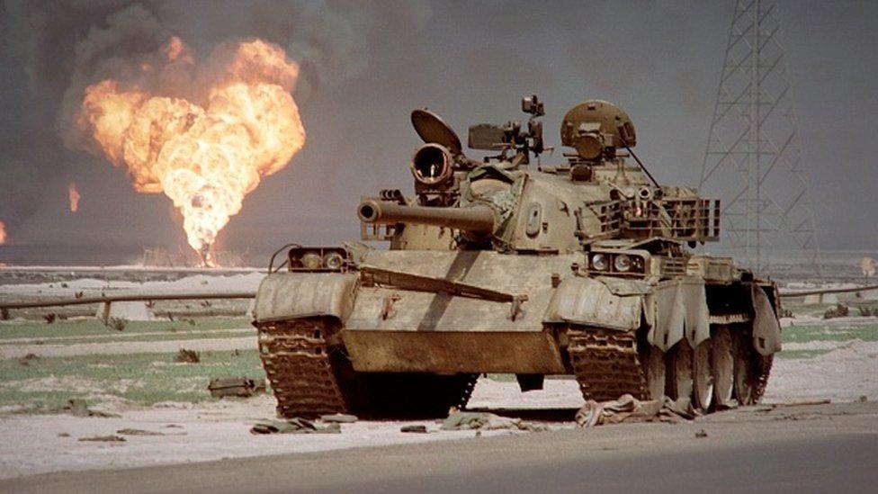 An abandoned Iraqi Soviet-made tank sits in the Kuwaiti desert in 1991 as an oil well at the Al-Ahmadi oil field is burning.