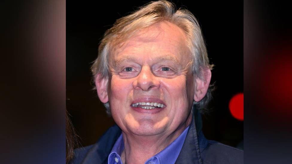 Martin Clunes seen in a picture, wearing a light blue shirt and a darker blue jacket 