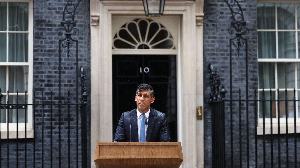 rishi sunak standing outside number 10 downing street behind a podium