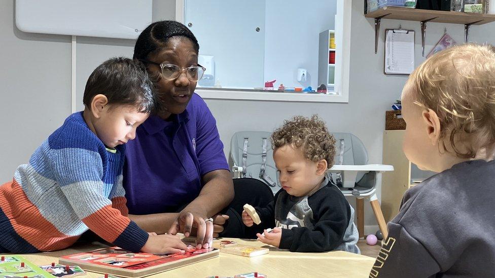 Nursery worker plays at table with three toddlers