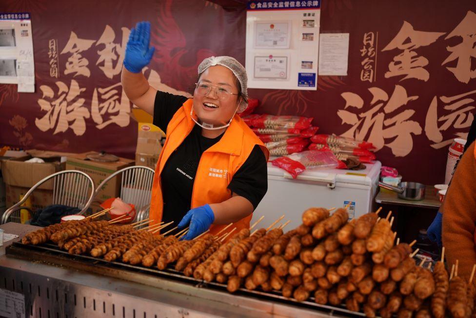 Woman working on food stall waving at someone off camera