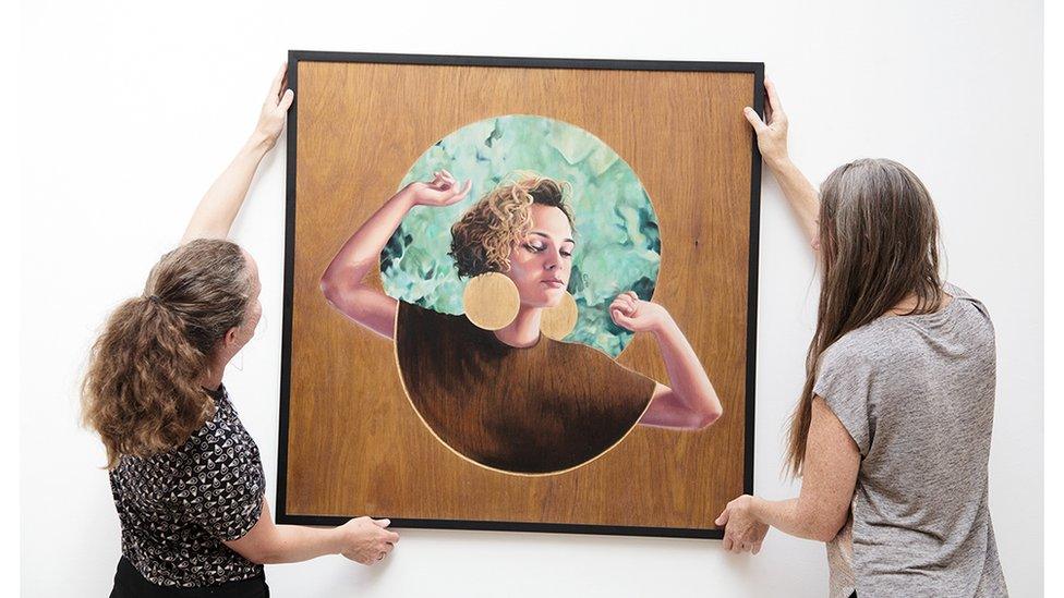 Two women holding a framed painting of a woman