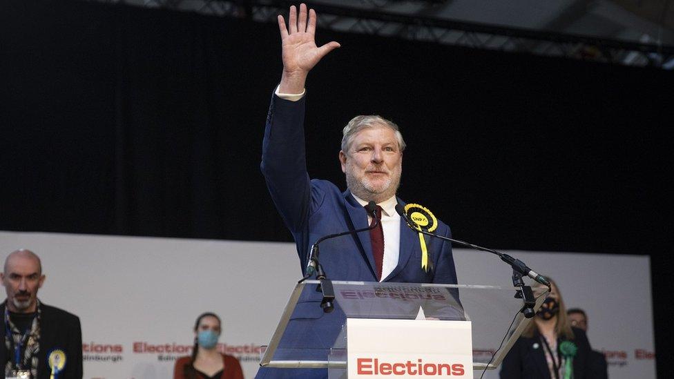 SNP candidate Angus Robertson stands on the stage with a hand waving, while the other candidates stand behind him