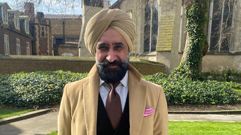 Pharmacy - Max Punni - a man in a tan-coloured turban and coat standing outside looking to the camera