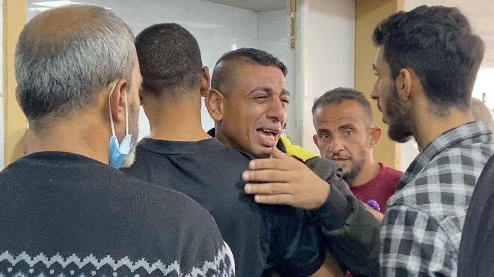 An emotional man is comforted by other men at the Kamal Adwan Hospital