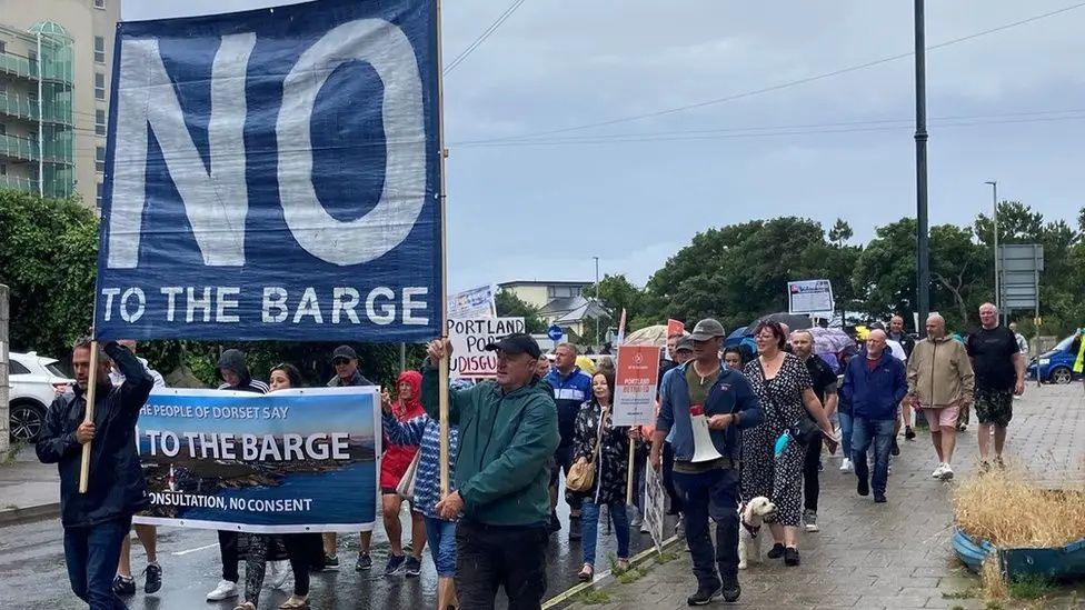 Protesters behind a banner saying 'NO to the barge'