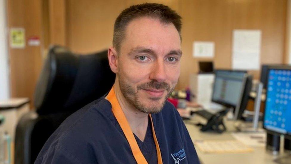 looking into the camera wearing an orange lanyard and navy scrubs