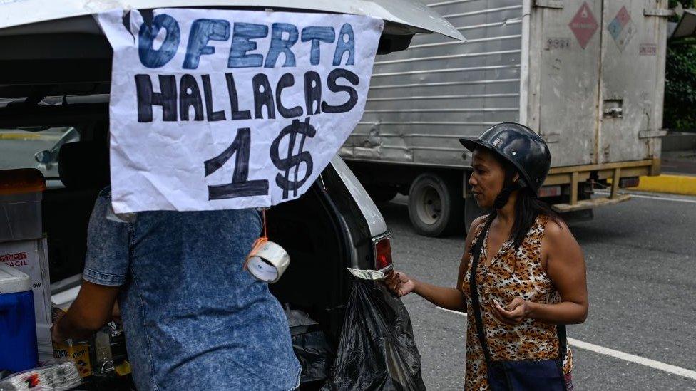 A woman buys a "hallaca" -typical venezuelan Christmas dish- with US dollars in a street of Caracas on November 19, 2019.