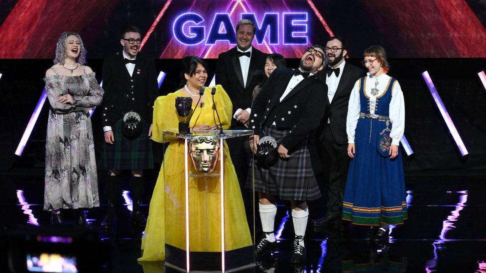 A team celebrates wining an award on stage, with some dressed in kilts and traditional Scottish outfits