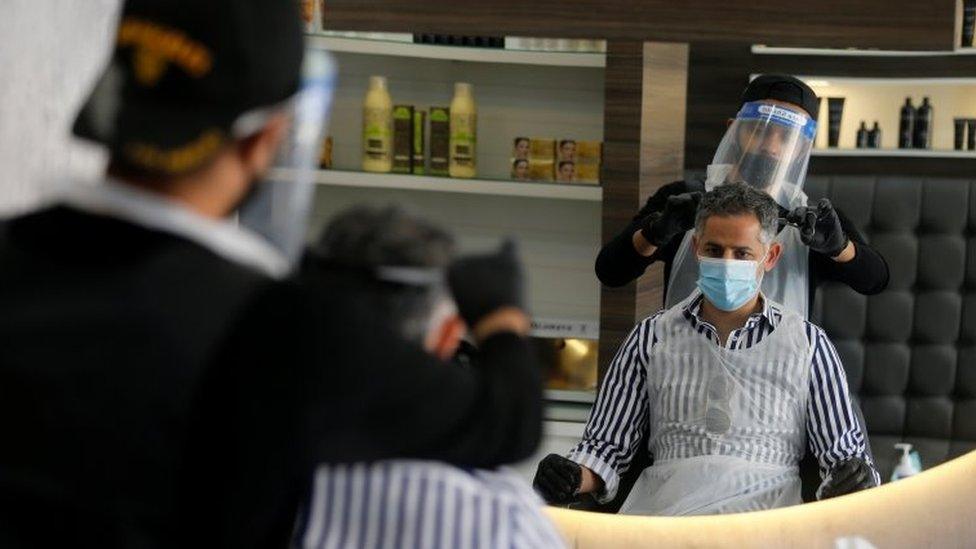 A man has his hair cut by a barber wearing protective equipment in Isa Town, Bahrain (27 May 2020)