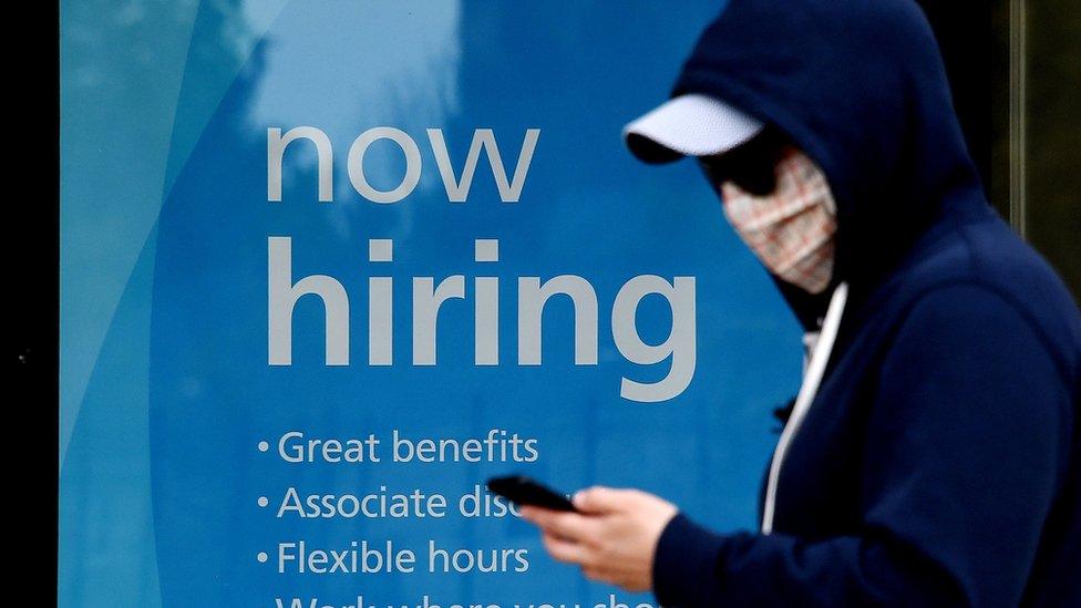 man wearing a face mask walks past a sign "Now Hiring" in front of a store amid the coronavirus pandemic on May 14, 2020 in Arlington, Virginia.