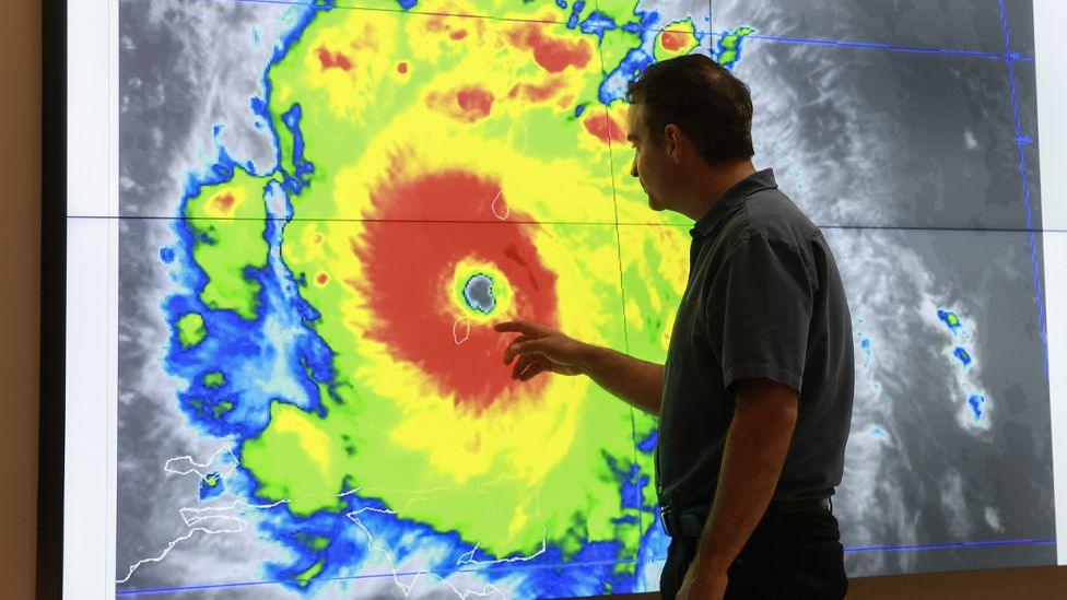 A man inspects a false colour satellite image of Hurricane Beryl on a giant screen at the National Hurricane Center in Florida, run by the NOAA. 