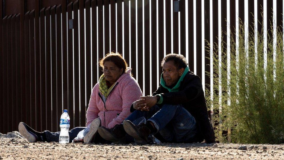 Two migrants sit on the ground near the border between the US and Mexico