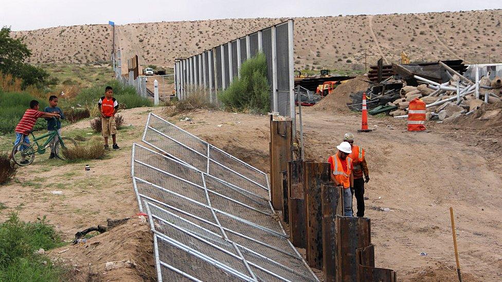 Construction workers assemble a portion of a border wall between the US and Mexico.