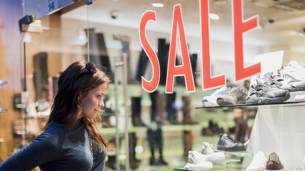 Woman looking in a shop window with a sale sign