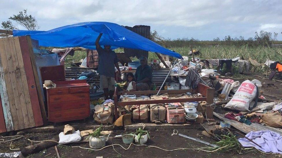 Residents taking shelter under a plastic sheet among the ruins of their house (22 February 2016)