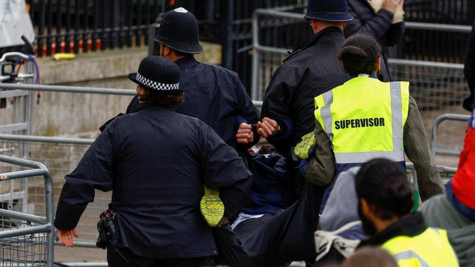 Police detain a protester, with three officers and one supervisor are holding a handcuffed person by each limb and carrying them away