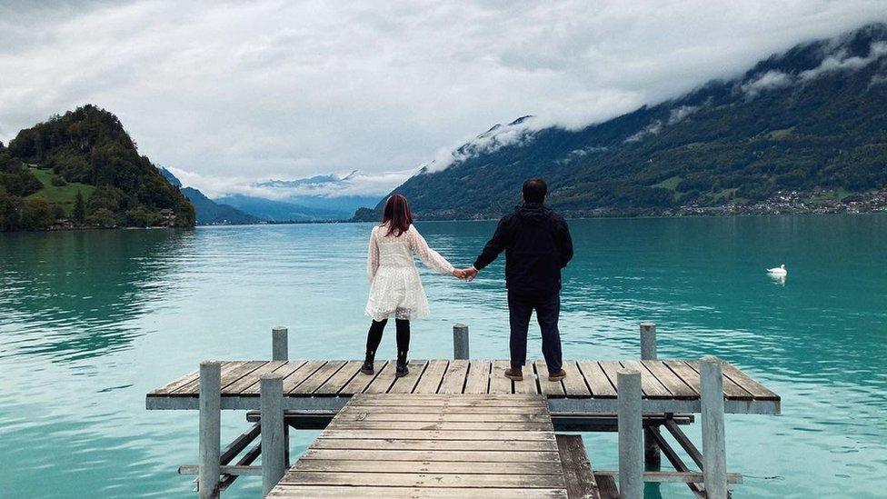 A couple stand, holding hands on the landing pier in Iseltwald