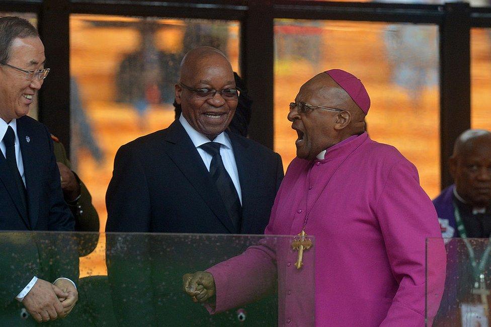 South African Archbishop and Honorary Elders Desmond Tutu (R) shakes hands with UN Secretary General Ban Ki-moon (L) and South Africa's President Jacob Zuma (C) during the memorial service of South African former president Nelson Mandela at the FNB Stadium (Soccer City) in Johannesburg on December 10, 2013.