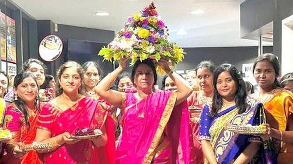 Women in colourful sarees holding a flower stack