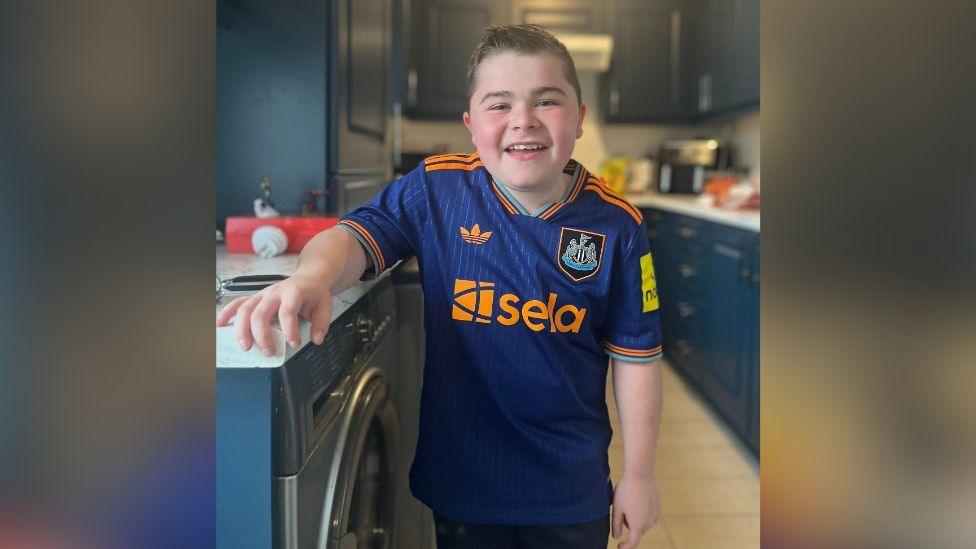 Alfie Pentony, in blue Newcastle United football shirt, resting his arm on a washing machine.