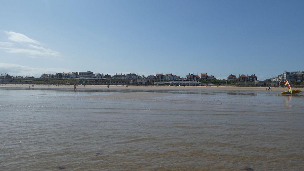 A view from the sea showing Bridlington South Beach with beach huts by the shore and people paddling