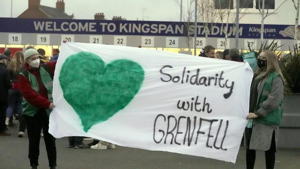 Protesters opposing Ulster Rugby's sponsorship deal outside Kingspan Stadium in January 2022 holding a large 'solidarity with grenfell' banner featuring a green heart