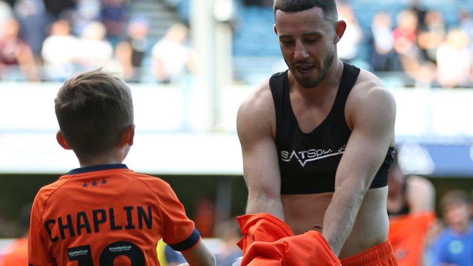 Conor Chaplin takes off his shirt to give to a young mascot