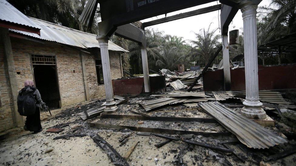 A woman walks next to a burned Church in Aceh Singkil, Indonesia, on 14 October 2015