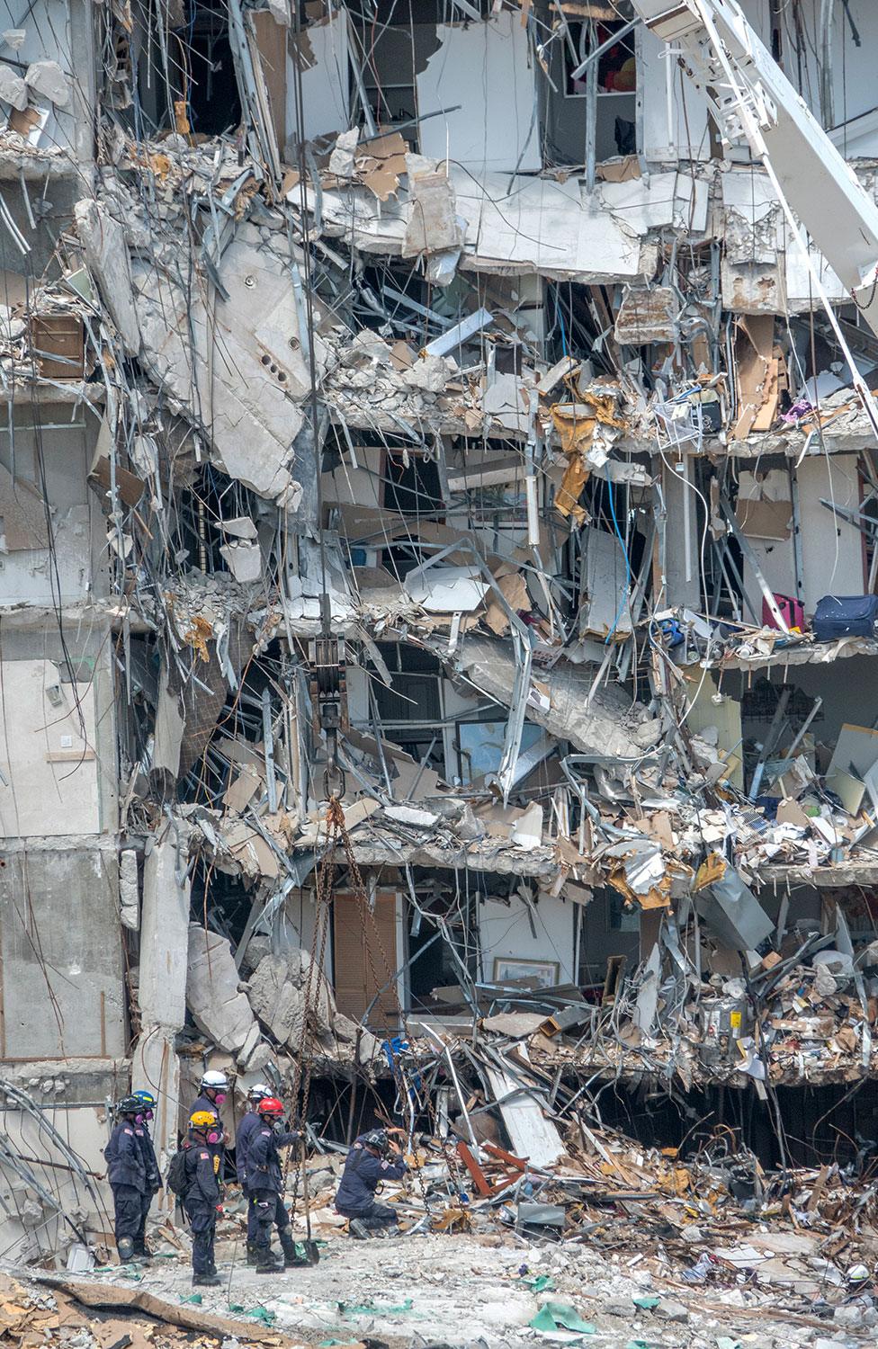 Rescue teams stand amid rubble of collapse building