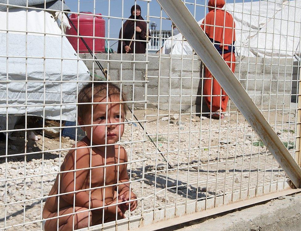 Child crouching behind a metal fence