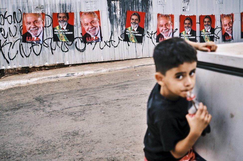 Boy drinks cola in Brasilia with Lula posters behind