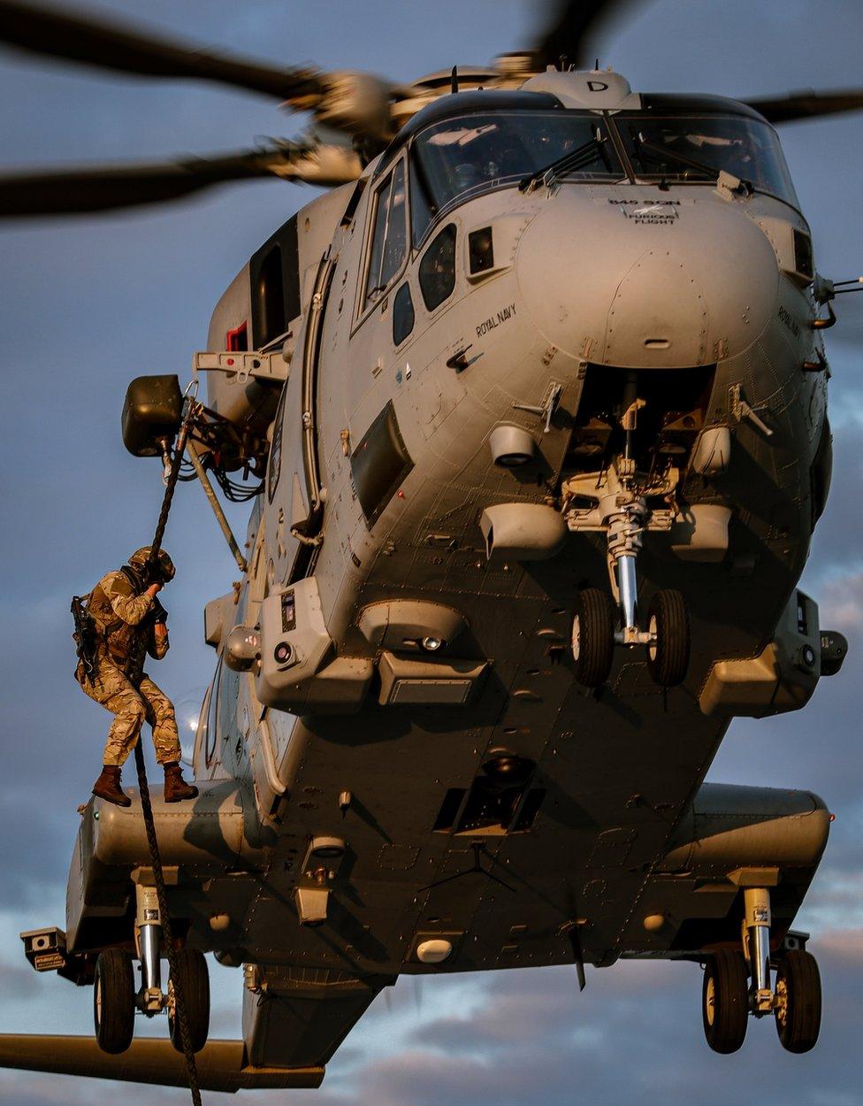 A Royal Marine dangles from a helicopter from a rope