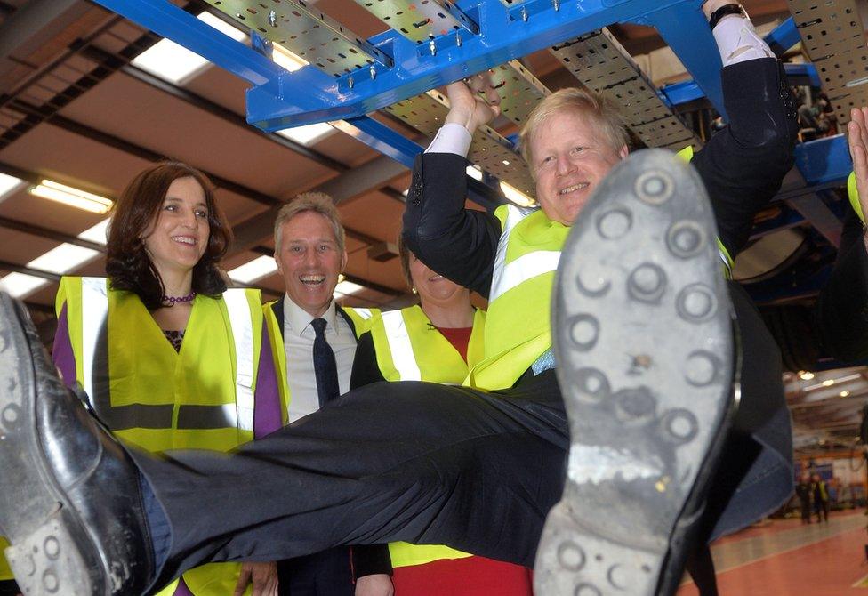 Boris Johnson swings from the undercarriage of a bus under construction during his February 2016 visit to a Wrightbus factory in Northern Ireland