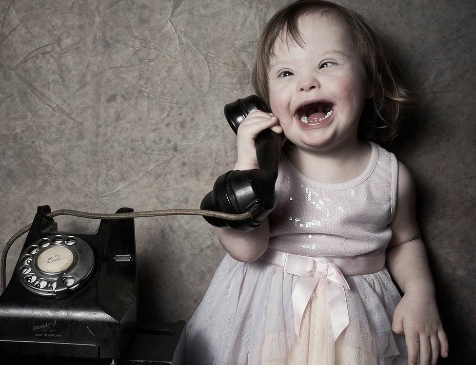 A young girl pretends to speak on an old telephone