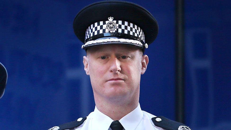 Steve Rodhouse, a clean-shaven Caucasian male, wearing a white police shirt with police issue epaulettes, a black tie and police hat.