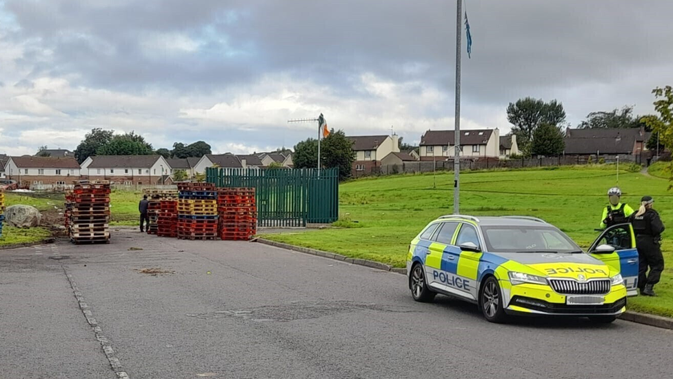 Police officers and a police car close to bonfire site in Galliagh in Londonderry where wooden pallets have been stacked