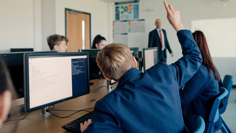 A boy putting his hand up in the classroom